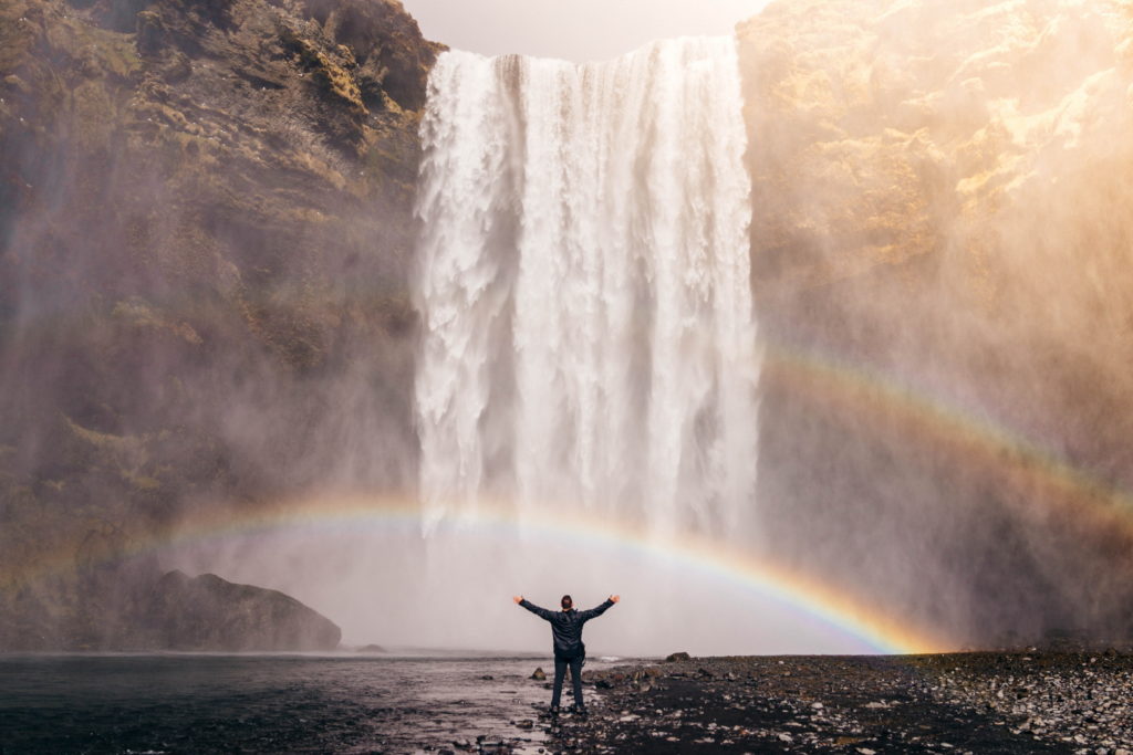 Man standing in front of waterfalls with double rainbow in Iceland