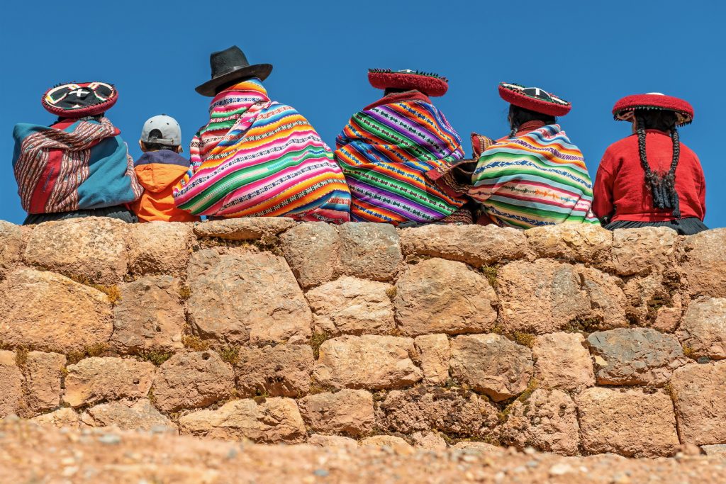 A group of indigenous Quechua women in traditional clothes sitting on an ancient Inca wall in Peru