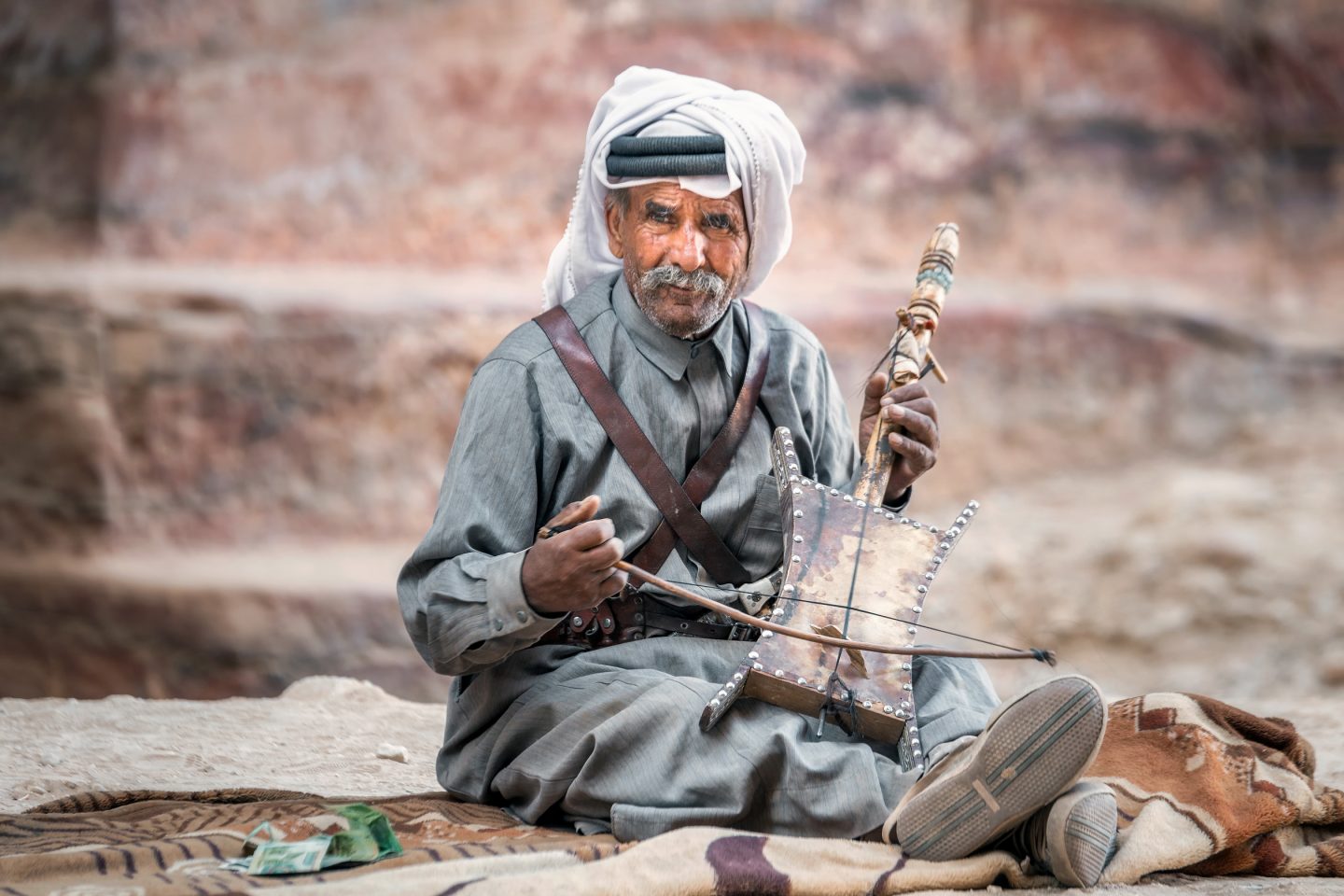 A local Bedouin sitting on the floor with an instrument in Petra, Jordan
