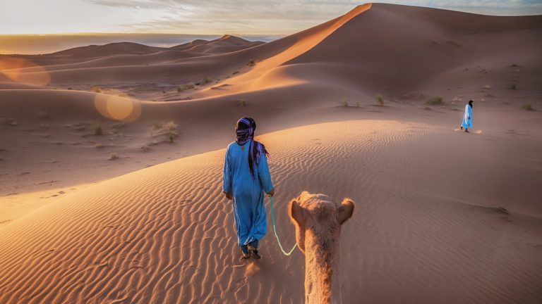 Two Tuareg nomads lead a camel in the Sahara, Morocco.