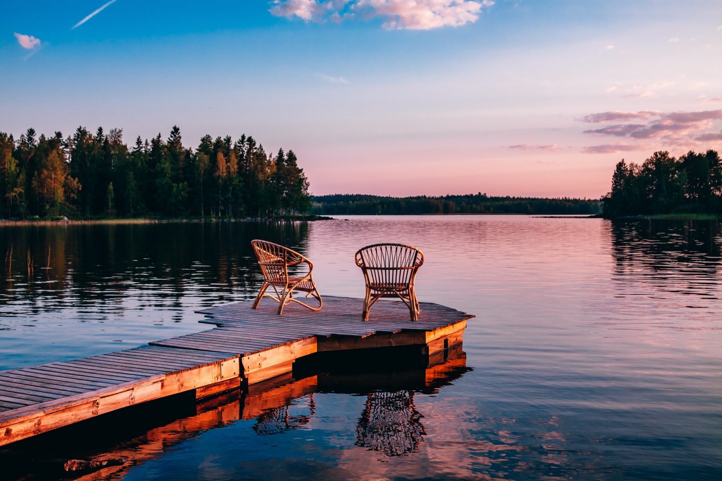 Two wooden chairs on a pier overlooking a lake at sunset in Finland