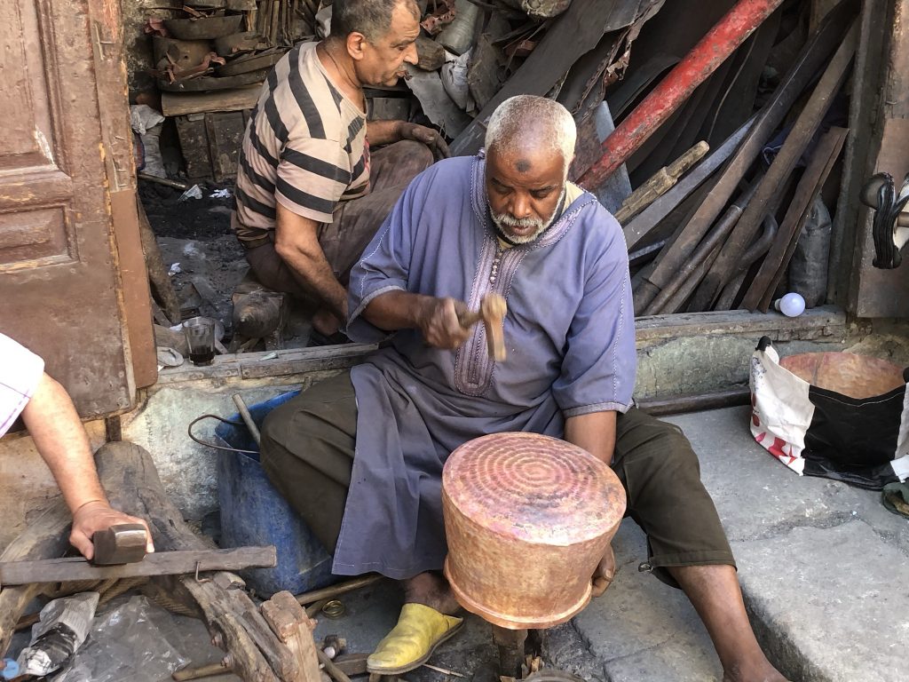 Metalworkers hammering out huge copper pans in Fez, Morocco.
