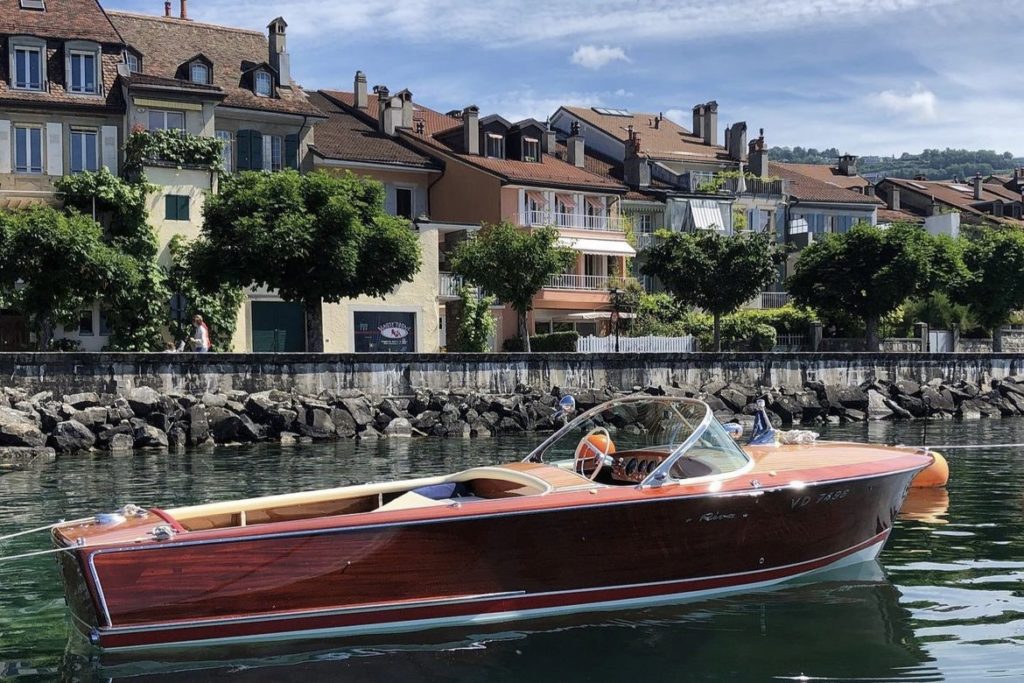 The iconic Riva boat on the shores of Lake Geneva, its elegant silhouette framed against a backdrop of charming lakeside houses.