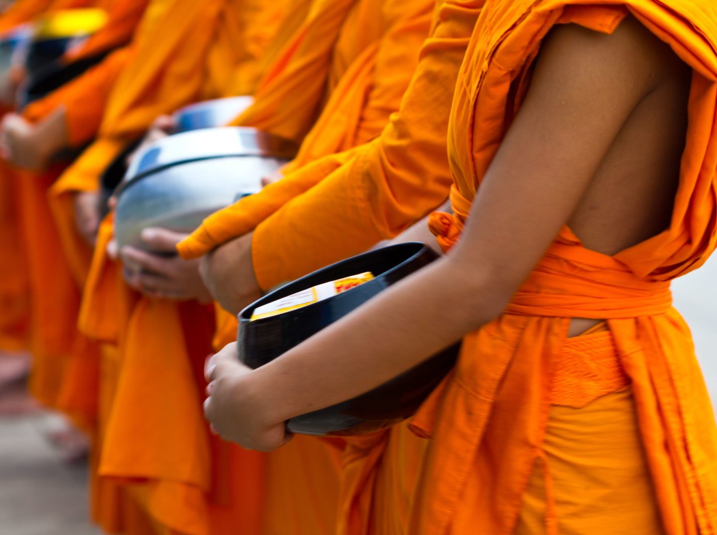 Long line of begging bowls awaiting rice donations to support the monks' spiritual quest in Battambang, Cambodia