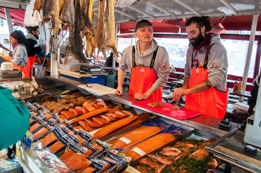 Two sellers of fresh fish at the fish market in Norway dressed in red aprons.