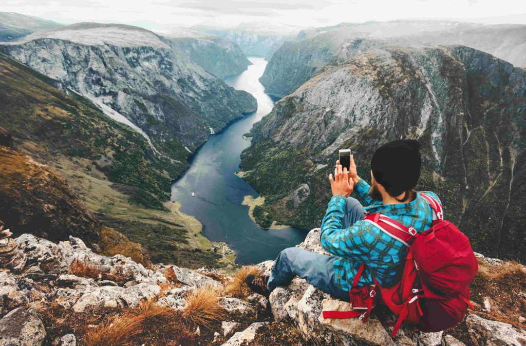 Backpacker with smartphone relaxing on a mountain top in Norway overlooking the fjords