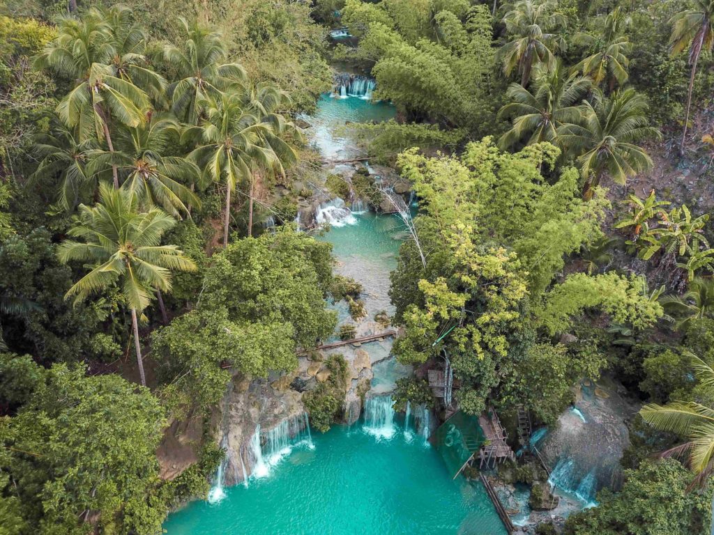 Aqua blue waters cascade beneath lush green trees at a stunning waterfall in Siquijor the Philippines.