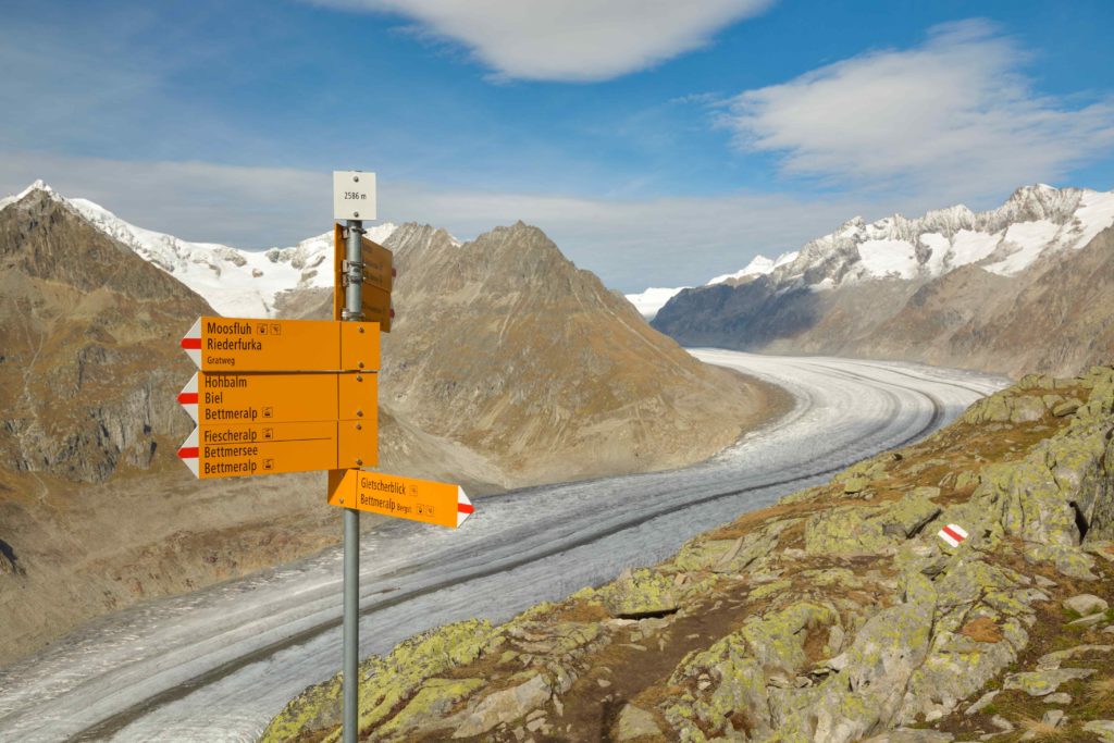 A picturesque scene in the Alps with a signpost, set against the stunning backdrop of the majestic Aletsch Glacier