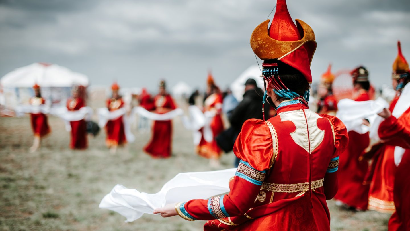 People in red costumes with golden hats, holding white cloths in their hands, performing a ritual.