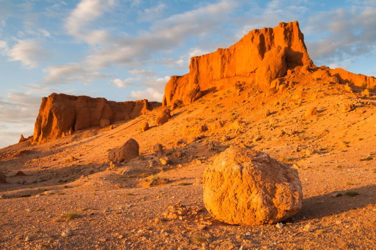 A rocky desert landscape with a large boulder and cliffs.