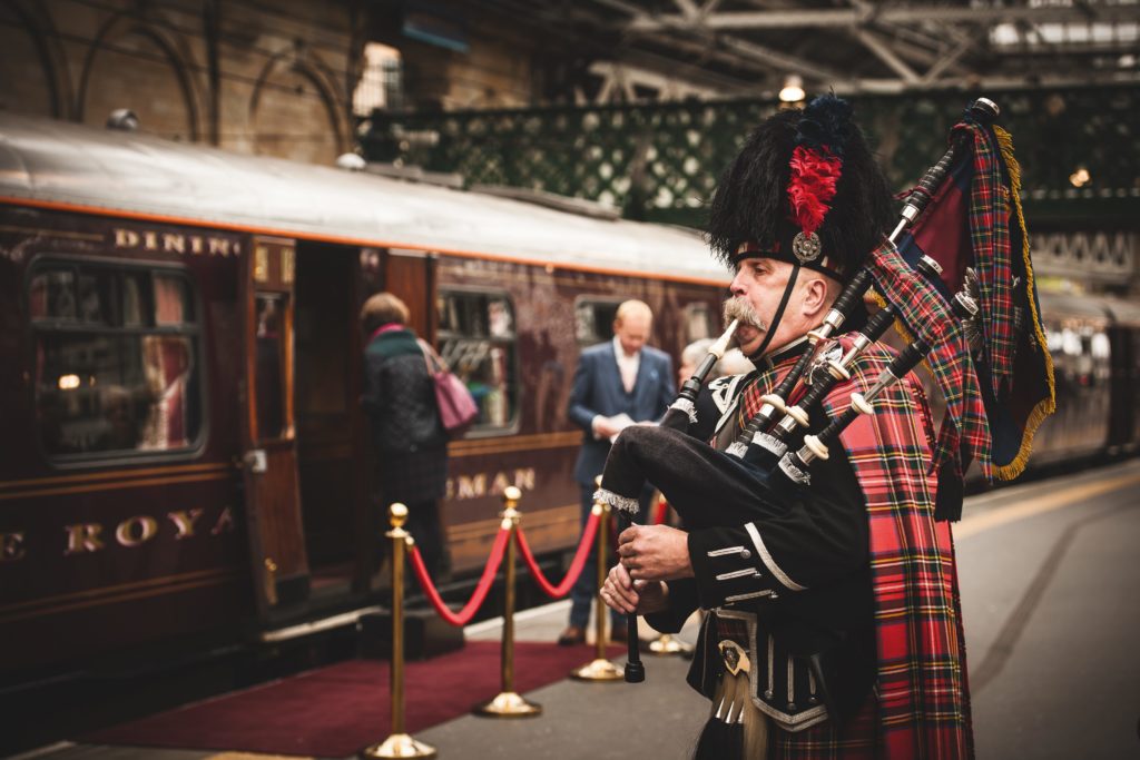 Enchanting image of the Royal Scotsman train in Scotland, complemented by a kilted piper adding a touch of tradition and flair.