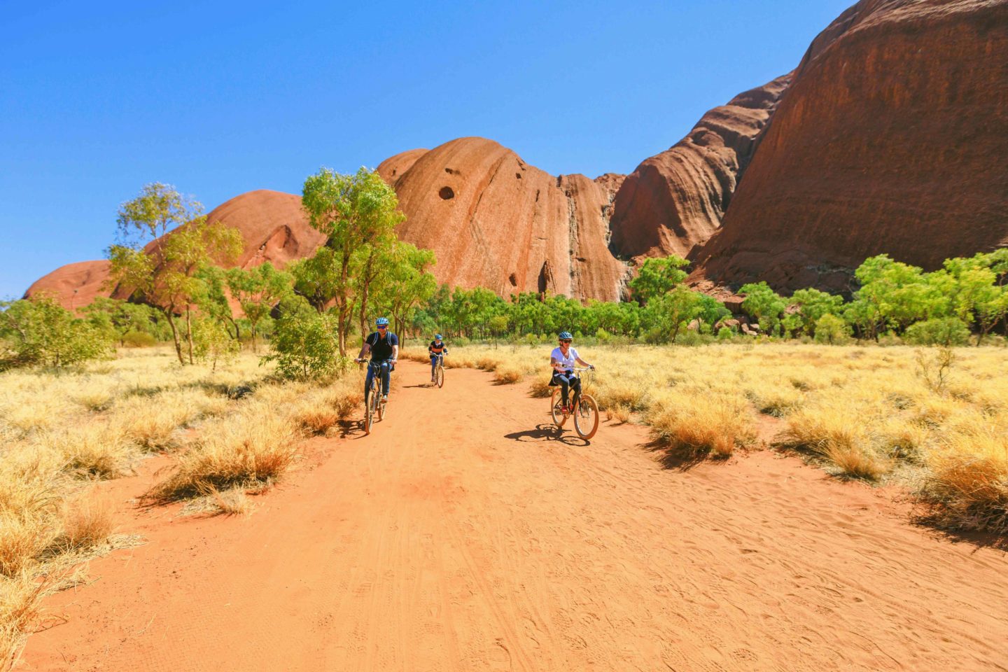 A group of cyclists on a dirt path with red rock in background.