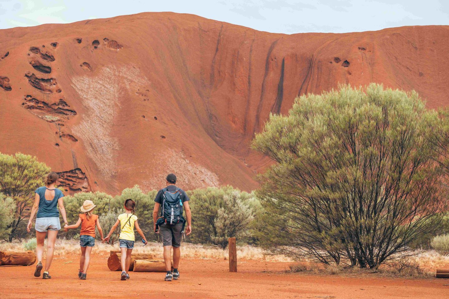 Family walking towards a large red rock formation in the Australian outback.