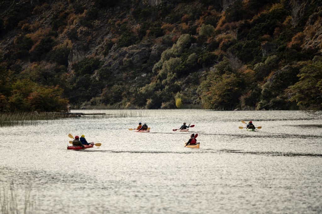 A group of kayakers on a serene lake, with lush mountains and reeds around them.