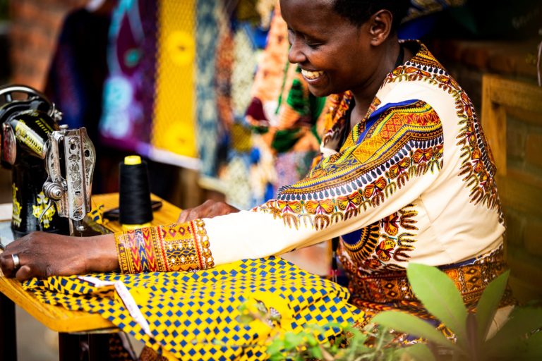 A woman sewing a colorful geometric fabric with a sewing machine on a wooden table.