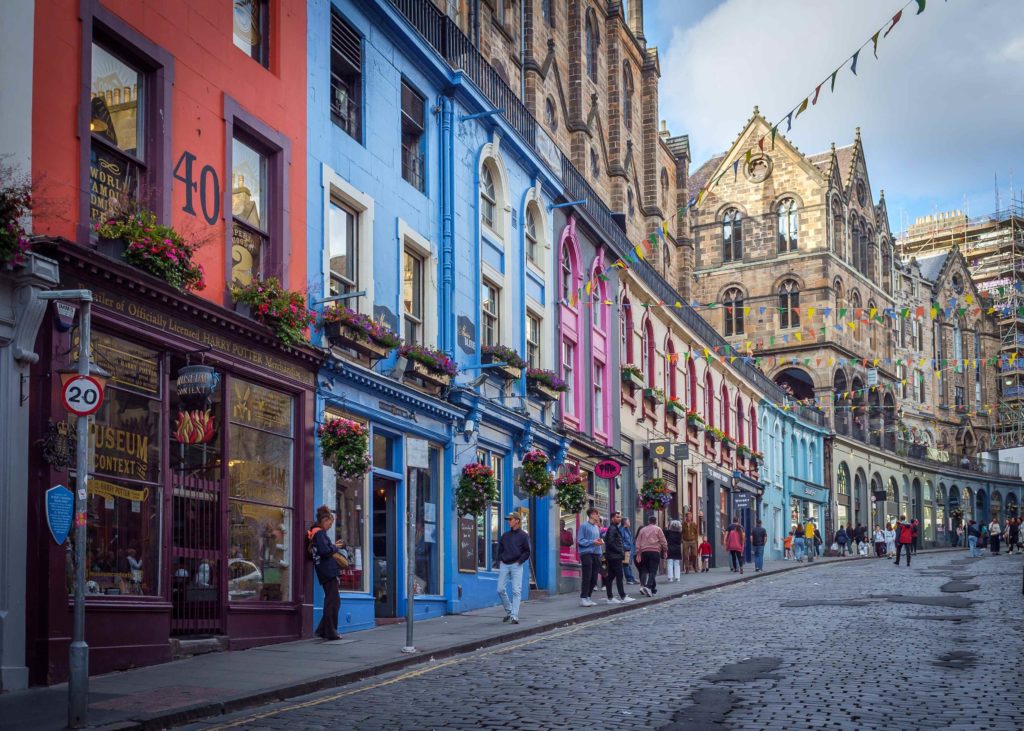 Edinburgh's Victoria Street features a beautiful curve, vibrant shopfronts, open-air cafes, and people leisurely strolling by.