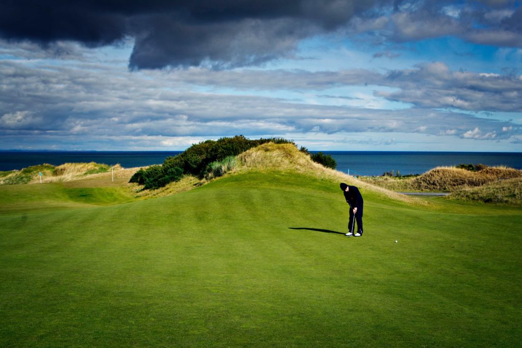 Scenic view of the Old Course at St. Andrews in Scotland, where golfers enjoy a round against a backdrop of lush landscapes.