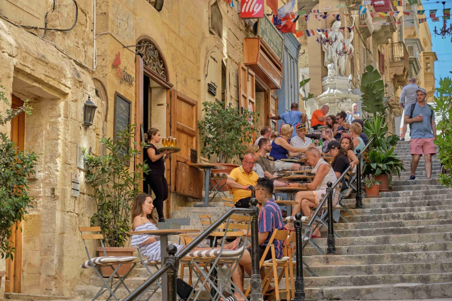 Tourists enjoying a break on the steps of the St. Lucia Street in Valetta, Malta.