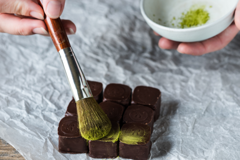 Max Chocolatier asting and making experience, showcasing the process of dusting matcha powder over pralines.