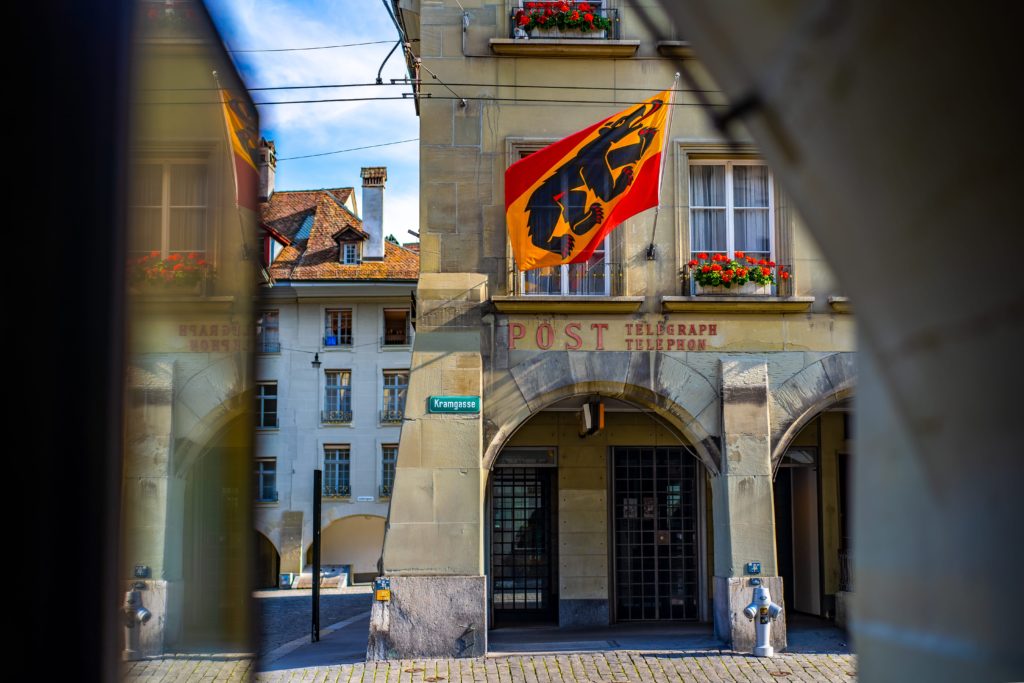 An elegant old building with inscriptions and a colorful flag, captured from a shaded viewpoint