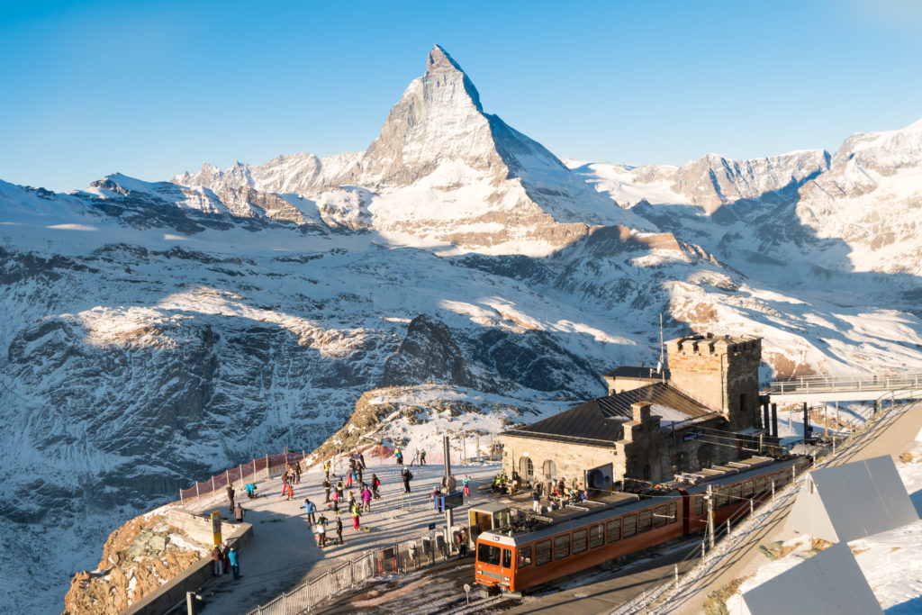Skiers and snowboarder gearing up at Gornergrat Bahn train station, Matterhorn peak providing a stunning backdrop to the ski track.