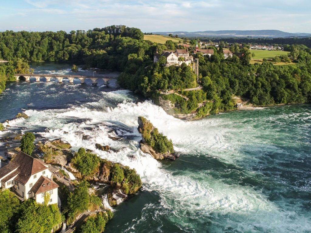 The powerful rush of water cascading amidst green landscapes and architectural beauty.