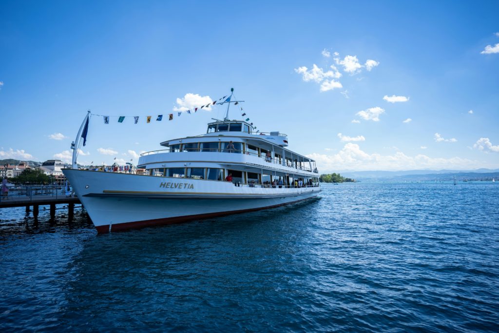 The Linth passenger boat at a pier on Lake Zurich, buildings of the city of Zurich in the background.