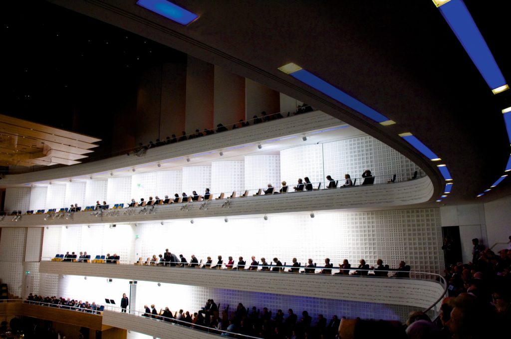 People fills a spacious building seated on the balcony creating a lively atmosphere.