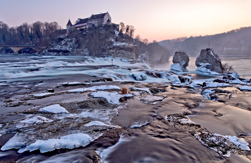 Landscape view of the Rhine Falls waterfallon a winter evening with snow falling