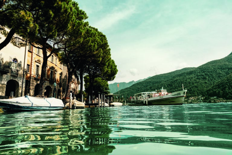 Calm waters reflecting the sky, with boats and a picturesque landscape in view.