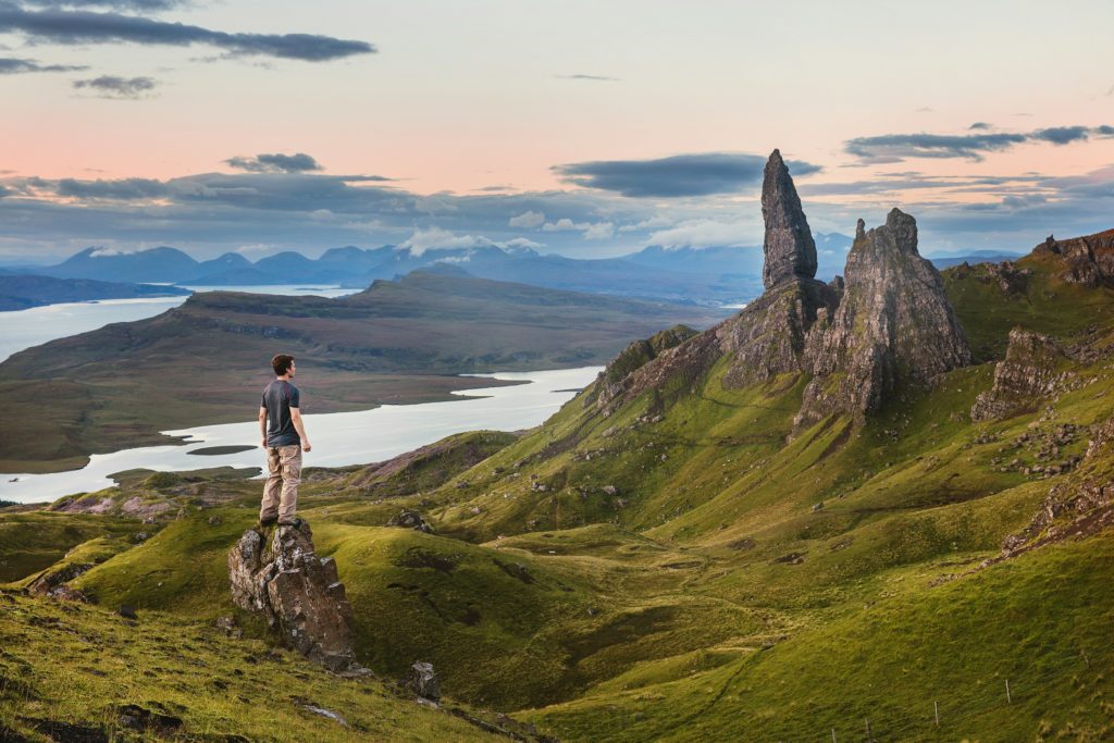 A man hiking up the steep path to Old Man Storr watching the sunrise, with the rocky hill and the early morning sky in view.