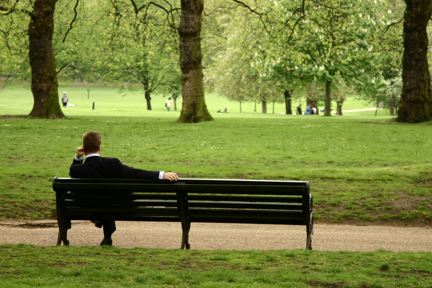 A person sitting serenely on a bench, gazing out at the surroundings in a peaceful park setting.