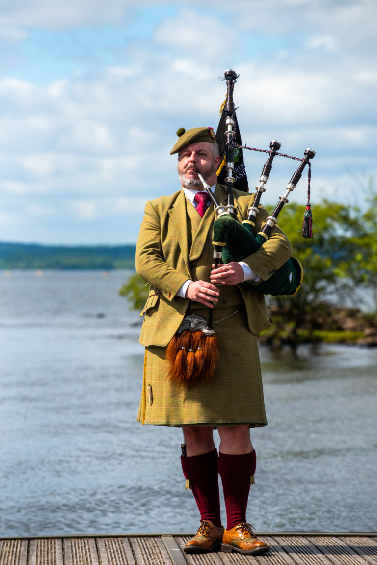 A bagpiper stands on a jetty by Loch Lomond during an event in Scotland.