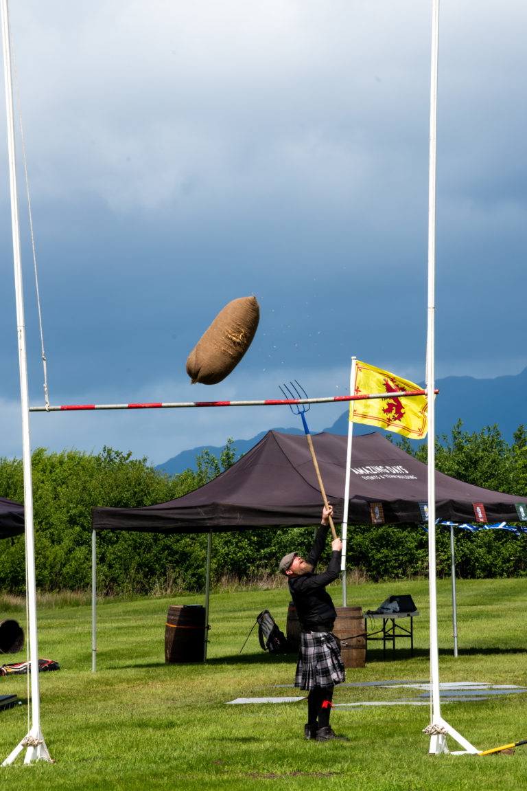 A man throws something high up with a pitchfork during an event in Scotland.