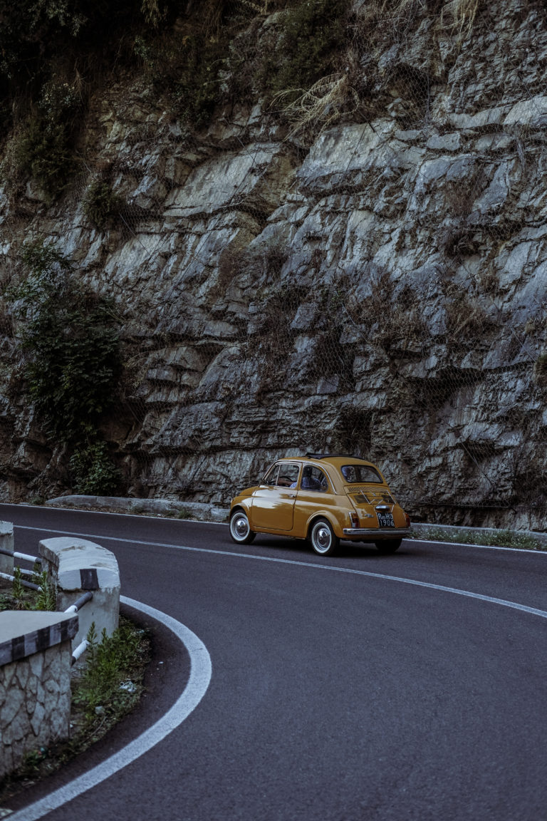 A classic orange Fiat 500 drives along the Amalfi Coast.