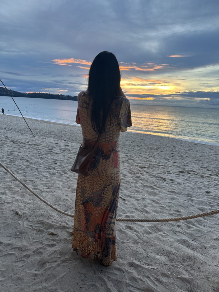 A woman takes a photo of the sunset on the beach in Phuket during an event.