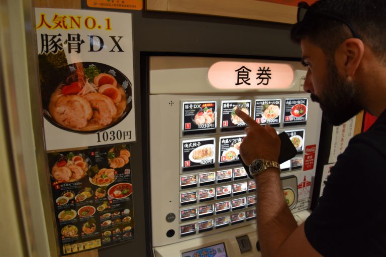 A man stands in front of a vending machine and orders food.