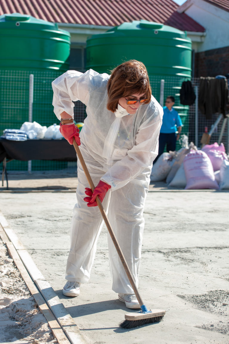 A woman in white coveralls sweeping the sidewalk