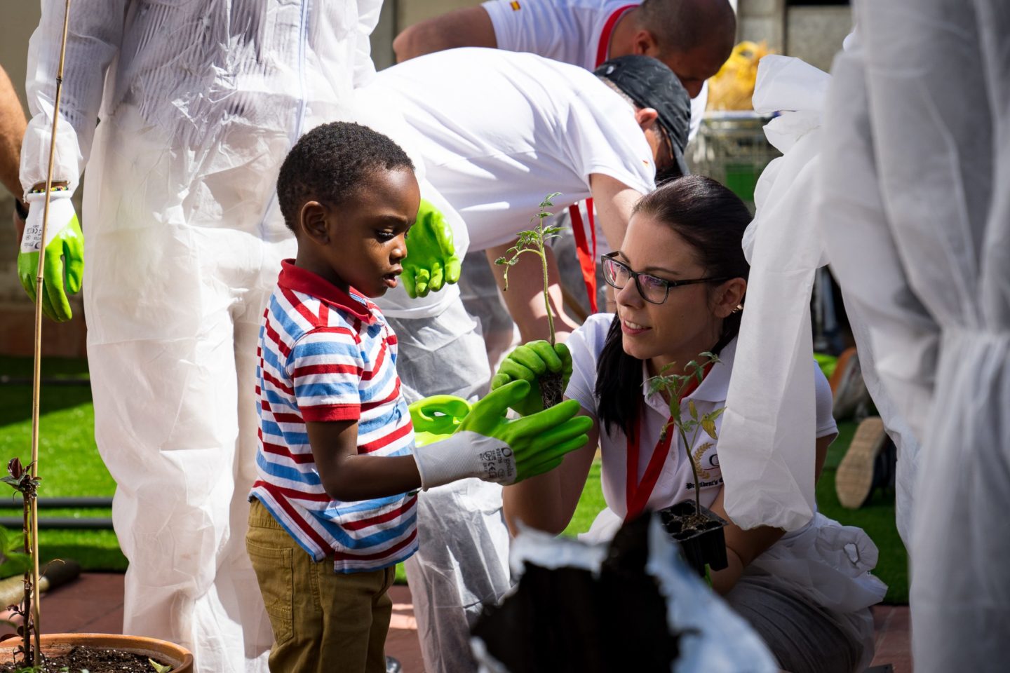 A woman hands a plant to a young boy during a CSR project in Madrid, Spain.