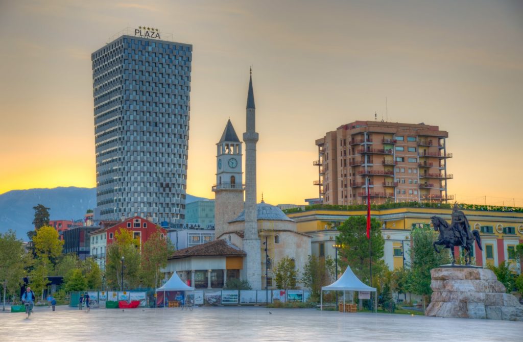 A vibrant city featuring a clock tower and a central fountain, highlighting the charm of Albania's capital and its eclectic attractions.