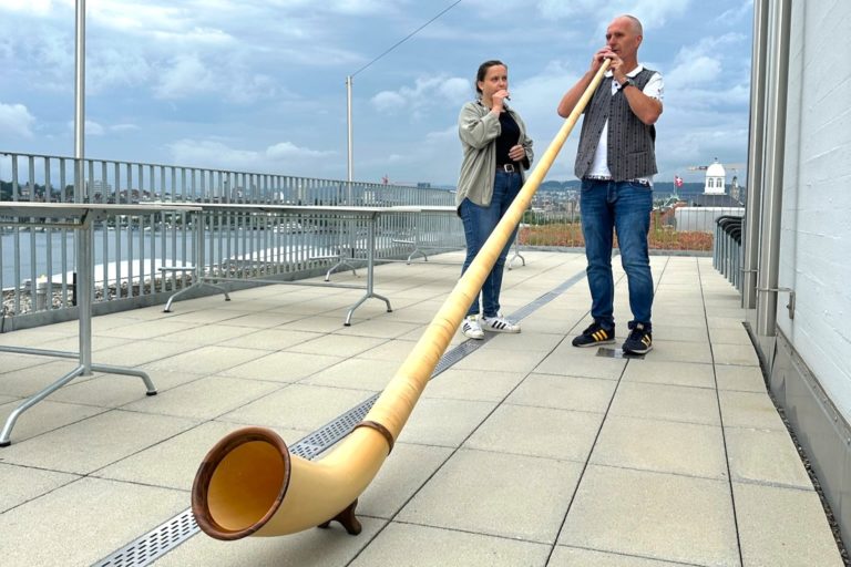 Two people on a lakeside rooftop in Zurich Switzerland playing the Alphorn