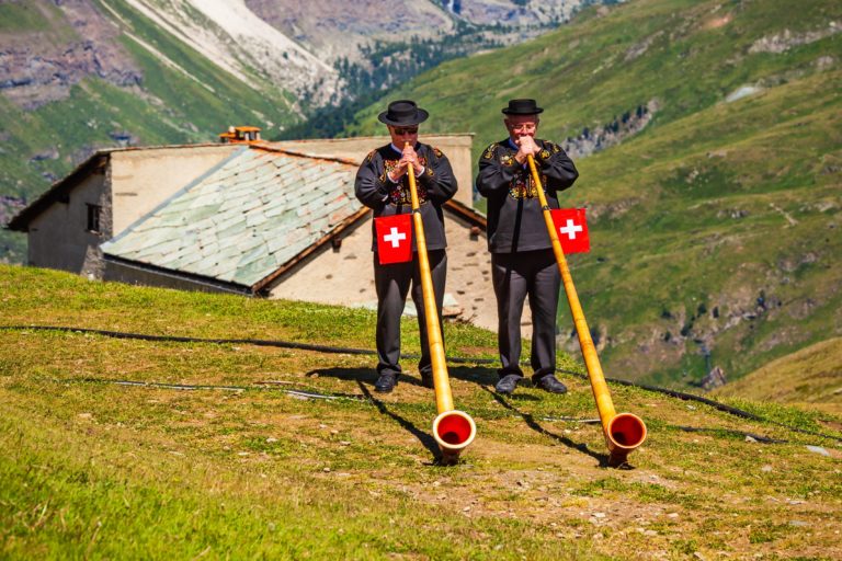 Two men in traditional swiss costumes playing the alphorn on mount Pilatus Switzerland