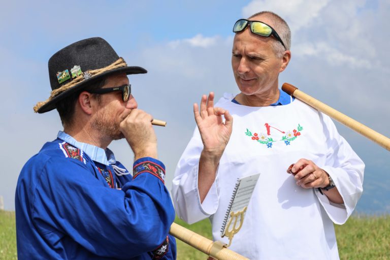 Two people in an alphorn workshop learning how to blow it