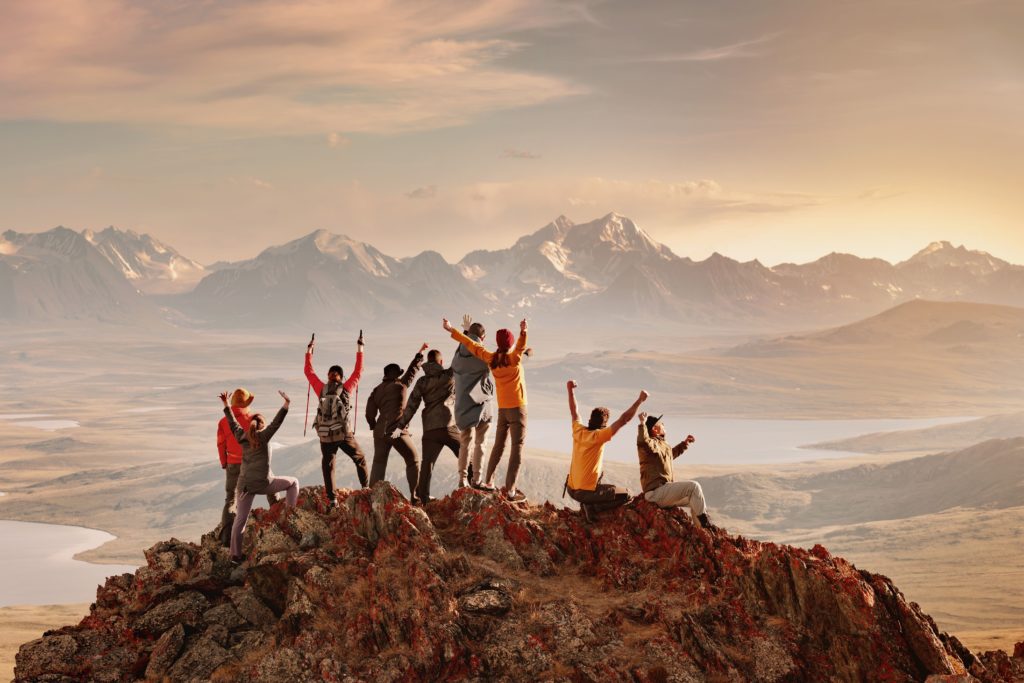 A group of friends standing on top of a mountain, celebrating their achievement with arms raised, surrounded by breathtaking panoramic views.