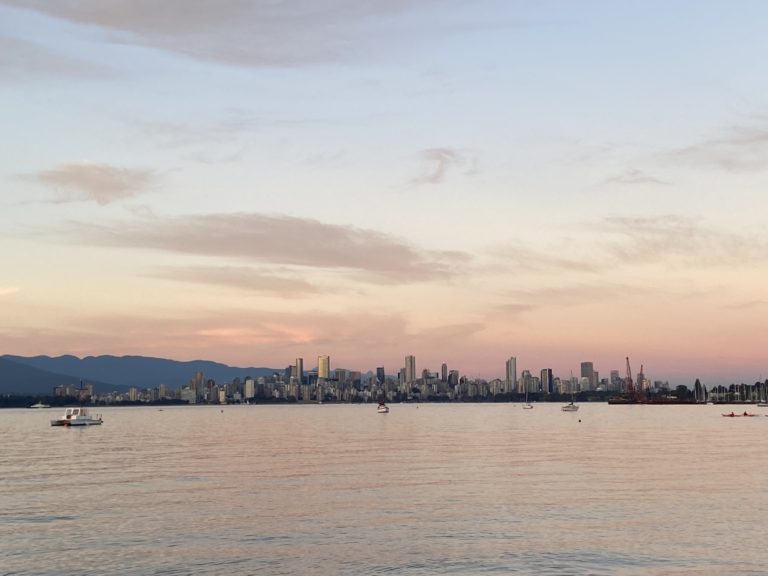 A panoramic view of the Vancouver skyline at sunset, with boats on the water