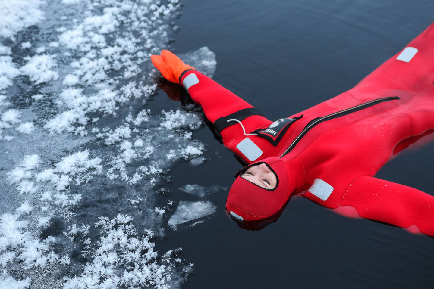 A person wearing a red survival suit floating in icy water