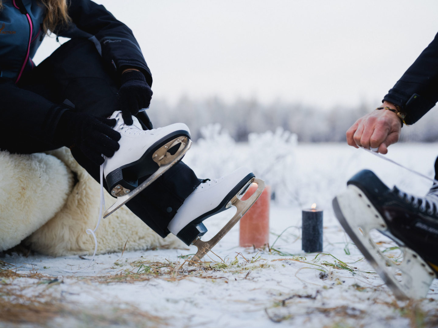 A winter scene with a person gearing up for ice skating on a frozen lake