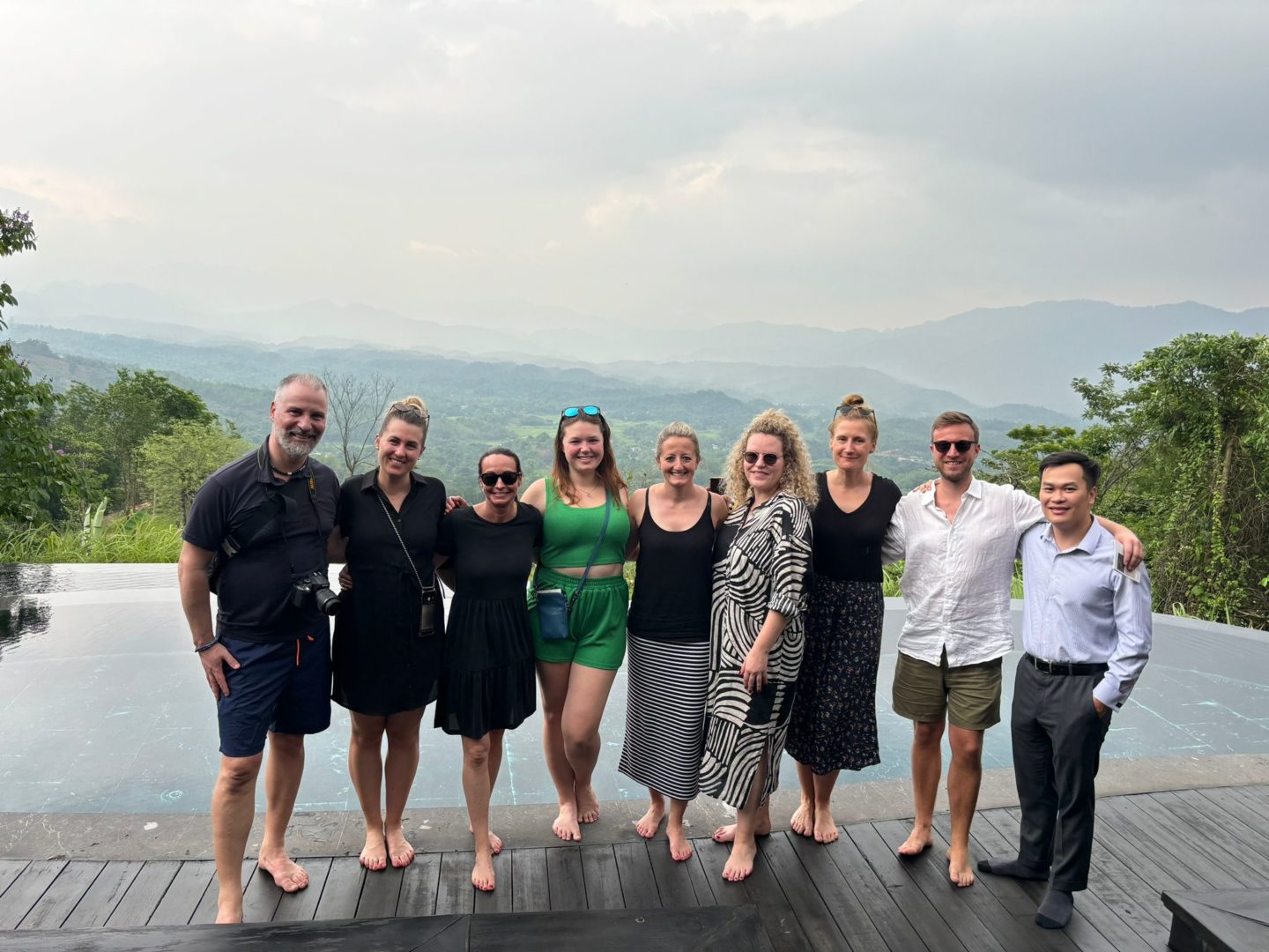 A group of people standing on a wooden deck, with mountains in the background in Hoi An