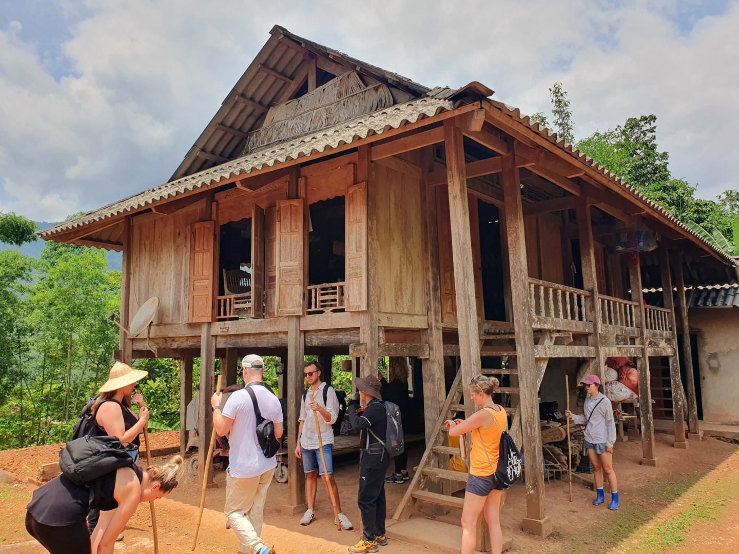 Trekkers pause outside a village wooden home, enjoying the sunshine