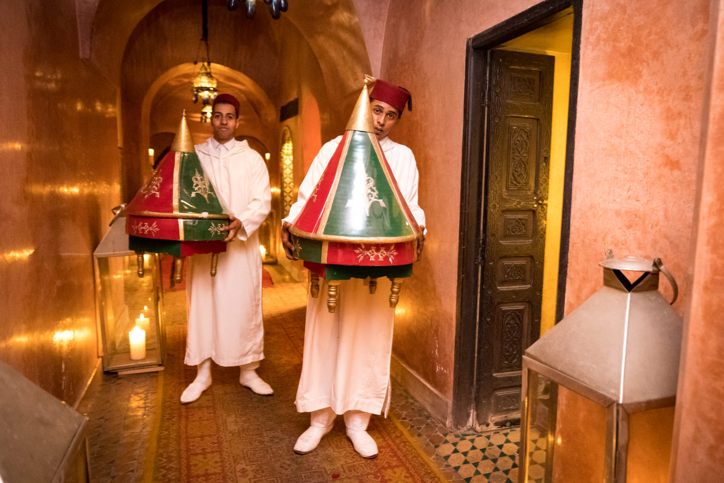 Hallway of Dar Yacut, two men in traditional attire carry colorful covered trays